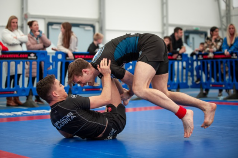 Two people in a no-gi BJJ match. One person is on the ground, thier guard is seemingly about to be passed by their opponent